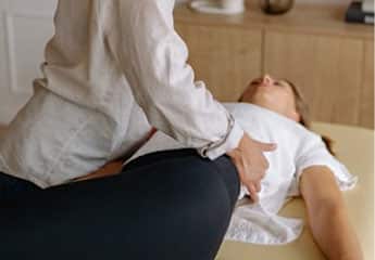 Therapist performing a hip stretch or manipulation on a patient lying on a treatment table.